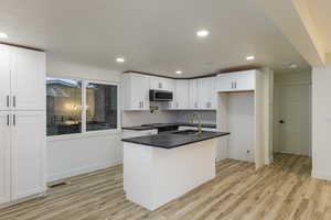 Kitchen featuring light wood-type flooring, sink, white cabinets, a center island with sink, and appliances with stainless steel finishes