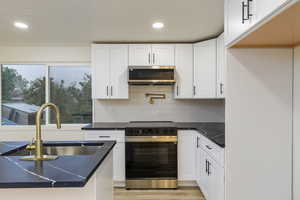 Kitchen featuring white cabinets, appliances with stainless steel finishes, and pot filler