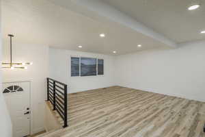 Interior space featuring a textured ceiling, light hardwood / wood-style flooring, beam ceiling, and a chandelier