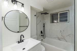 Full bathroom featuring a textured ceiling, vanity, toilet, and tiled shower / bath