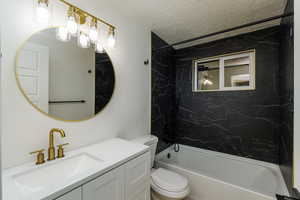 Full bathroom featuring a textured ceiling, vanity, toilet, and tiled shower / bath