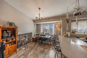 Dining area featuring a notable chandelier, wood-type flooring, natural light coming in east windows, open view through railing to family room