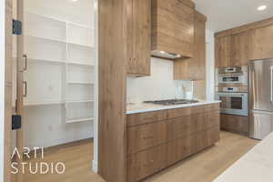 Kitchen with backsplash, appliances with stainless steel finishes, custom exhaust hood, and light hardwood / wood-style flooring