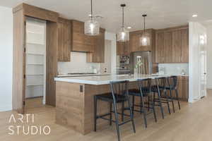 Kitchen with appliances with stainless steel finishes, light hardwood / wood-style floors, a breakfast bar, and hanging light fixtures