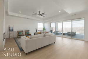 Living room with ceiling fan, a tray ceiling, light hardwood / wood-style flooring, and a healthy amount of sunlight