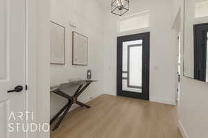 Foyer entrance with a high ceiling, light wood-type flooring, and an inviting chandelier