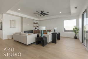 Living room with light hardwood / wood-style floors, ceiling fan, and a raised ceiling