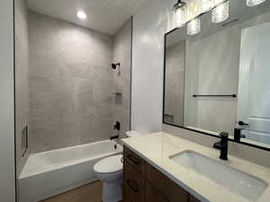 Full bathroom with vanity, tiled shower / bath, hardwood / wood-style flooring, and toilet