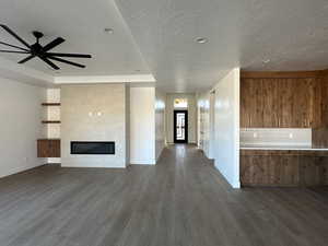 Unfurnished living room with ceiling fan, a large fireplace, a textured ceiling, and dark hardwood / wood-style flooring