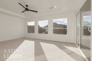 Empty room with ceiling fan, light colored carpet, plenty of natural light, and a tray ceiling