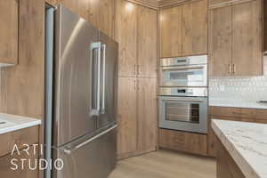 Kitchen featuring stainless steel appliances, light stone counters, backsplash, and light wood-type flooring