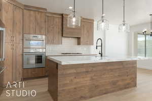 Kitchen featuring decorative light fixtures, tasteful backsplash, an island with sink, hardwood / wood-style flooring, and stainless steel double oven