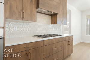 Kitchen featuring light hardwood / wood-style flooring, backsplash, custom exhaust hood, and stainless steel gas stovetop