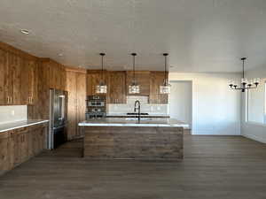 Kitchen with tasteful backsplash, pendant lighting, high end fridge, and a center island with sink