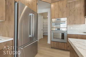 Kitchen featuring appliances with stainless steel finishes, light stone counters, light wood-type flooring, and decorative backsplash