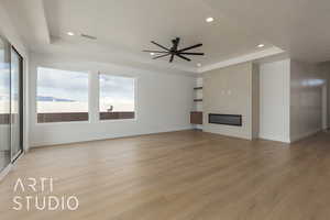 Unfurnished living room featuring a tray ceiling, light hardwood / wood-style floors, a large fireplace, and ceiling fan