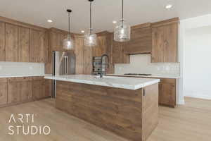 Kitchen featuring decorative light fixtures, stainless steel appliances, an island with sink, and light wood-type flooring