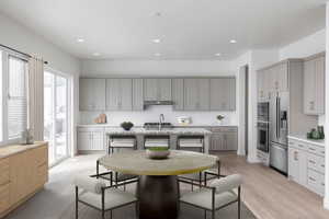 Kitchen with light hardwood / wood-style flooring, stainless steel appliances, gray cabinetry, a center island with sink, and light stone countertops