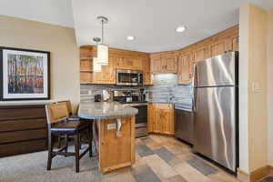 Kitchen featuring kitchen peninsula, hanging light fixtures, a kitchen breakfast bar, stainless steel appliances, and backsplash