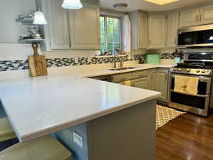 Kitchen with pendant lighting, sink, kitchen peninsula, stainless steel appliances, and dark hardwood / wood-style flooring