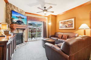 Carpeted living room featuring crown molding, a fireplace, and ceiling fan