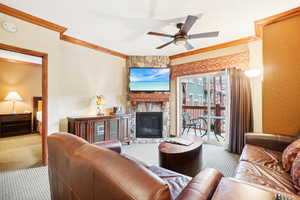 Carpeted living room with ceiling fan, crown molding, and a stone fireplace