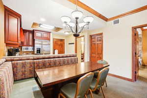 Dining space with crown molding, a tray ceiling, light carpet, and a chandelier