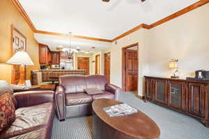 Living room with ceiling fan with notable chandelier, ornamental molding, and light carpet