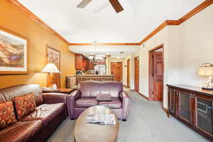 Carpeted living room featuring ceiling fan with notable chandelier and crown molding