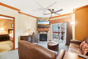 Carpeted living room featuring ceiling fan, a stone fireplace, and crown molding