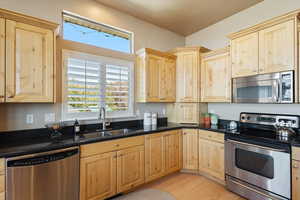 Kitchen featuring sink, light hardwood / wood-style flooring, light brown cabinets, appliances with stainless steel finishes, and dark stone countertops