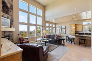 Living room with light wood-type flooring, sink, a fireplace, an inviting chandelier, and a towering ceiling