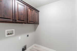 Washroom with light wood-type flooring, hookup for an electric dryer, washer hookup, and cabinets