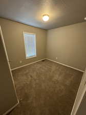 Spare room with a textured ceiling and dark colored carpet