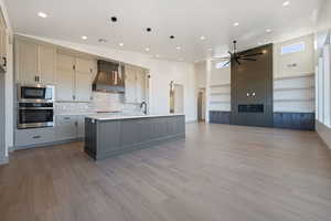 Kitchen with gray cabinetry, stainless steel appliances, premium range hood, pendant lighting, and a kitchen island with sink