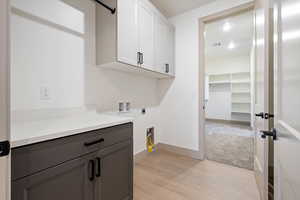 Laundry room with electric dryer hookup, cabinets, light hardwood / wood-style floors, and washer hookup