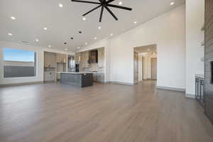 Unfurnished living room with ceiling fan, light hardwood / wood-style floors, sink, and high vaulted ceiling