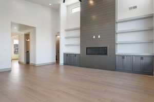 Unfurnished living room featuring light wood-type flooring, a towering ceiling, built in shelves, a large fireplace, and ceiling fan