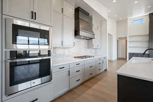 Kitchen with sink, light hardwood / wood-style flooring, custom range hood, appliances with stainless steel finishes, and white cabinetry