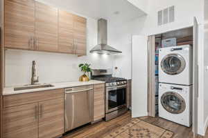 Kitchen featuring wall chimney exhaust hood, dark hardwood / wood-style flooring, stacked washing maching and dryer, and appliances with stainless steel finishes