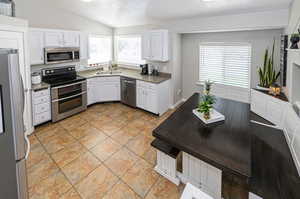 Kitchen featuring appliances with stainless steel finishes, vaulted ceiling, white cabinetry, and a wealth of natural light