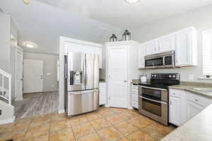 Kitchen featuring white cabinets, stainless steel appliances, light wood-type flooring, a textured ceiling, and lofted ceiling