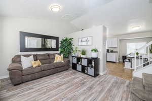 Living room with a textured ceiling, light hardwood / wood-style flooring, and lofted ceiling