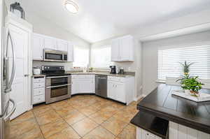 Kitchen featuring stainless steel appliances, white cabinetry, lofted ceiling, and a healthy amount of sunlight