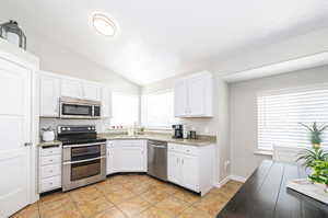 Kitchen featuring white cabinets, lofted ceiling, light tile patterned floors, sink, and stainless steel appliances