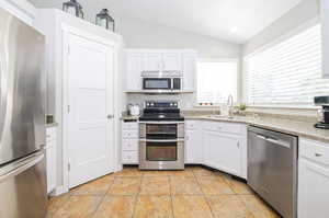 Kitchen with sink, stainless steel appliances, vaulted ceiling, and white cabinetry