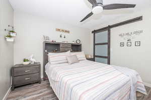 Bedroom with a barn door, light wood-type flooring, and ceiling fan