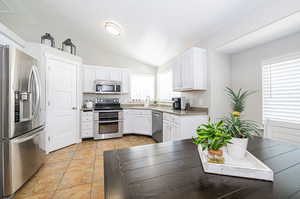 Kitchen with white cabinetry, vaulted ceiling, light tile patterned floors, stainless steel appliances, and sink