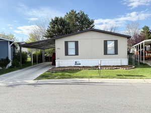 Manufactured / mobile home featuring a front lawn, an attached carport, and driveway