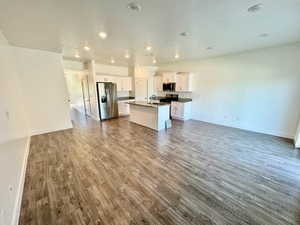 Kitchen with white cabinets, stainless steel appliances, hardwood / wood-style flooring, a center island with sink, and sink